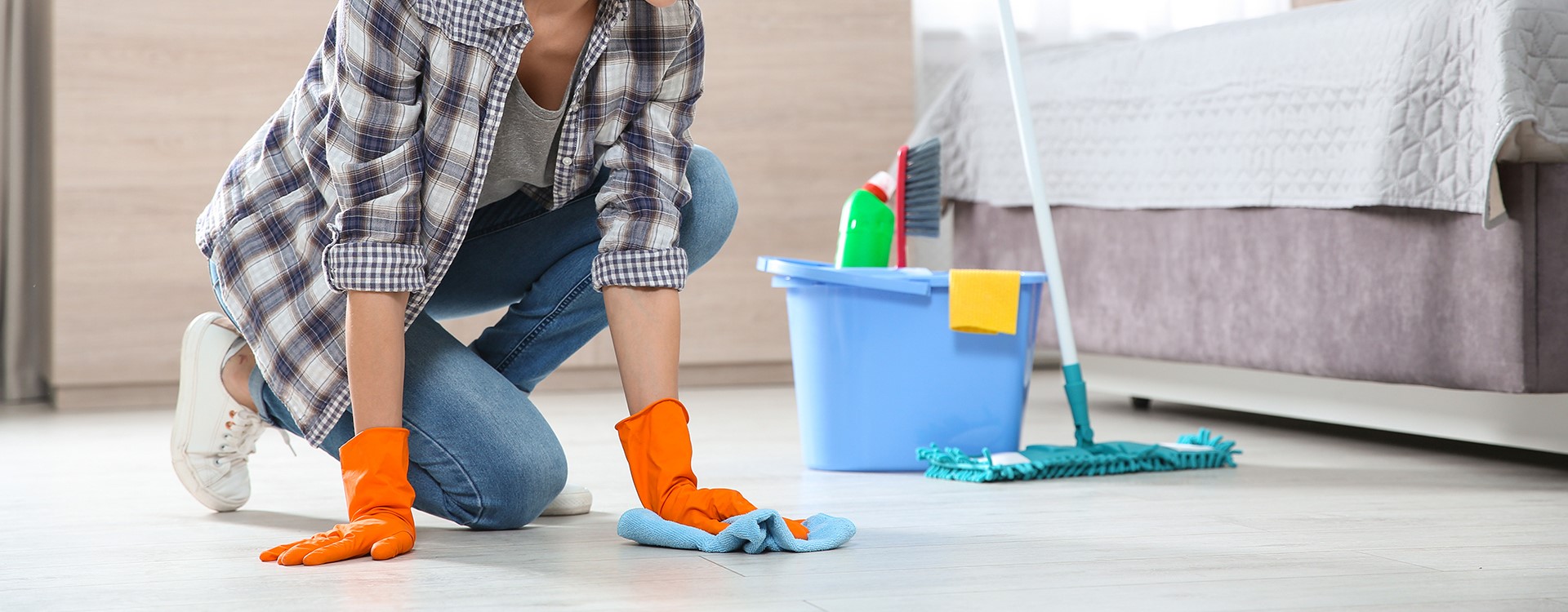 A person wearing orange gloves kneeling down to wipe down the floor of a bedroom