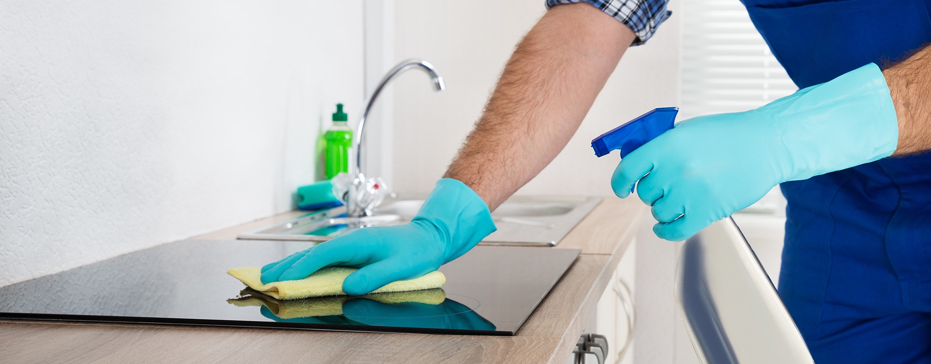 A person wearing turquoise gloves spraying and wiping down a ceramic cooktop