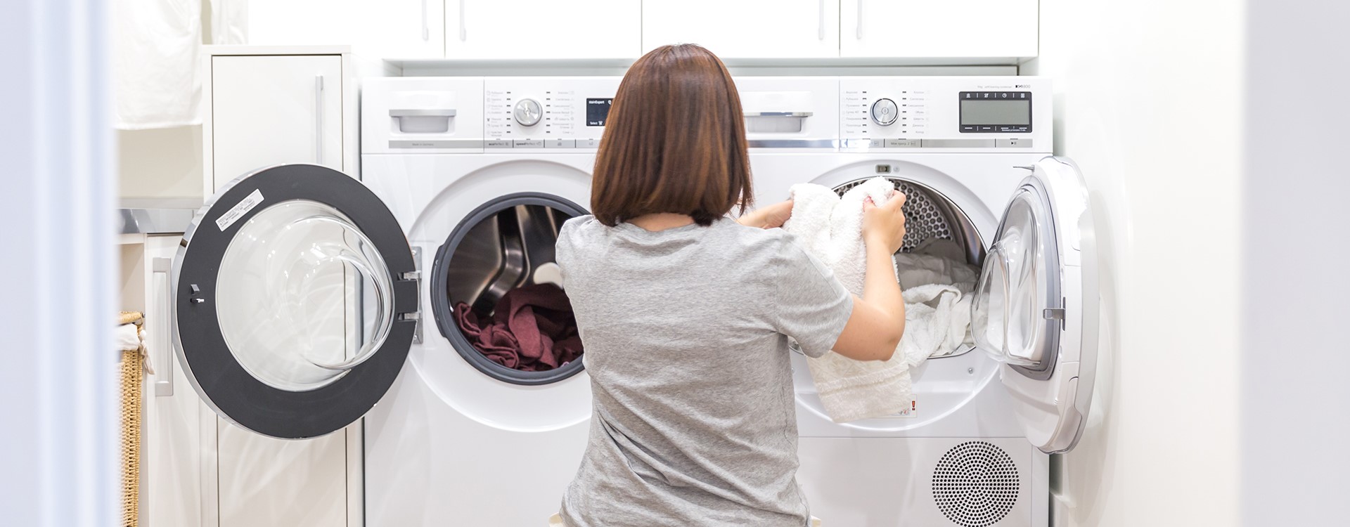 A person moving laundry from a front-load washing machine to a front-load dryer